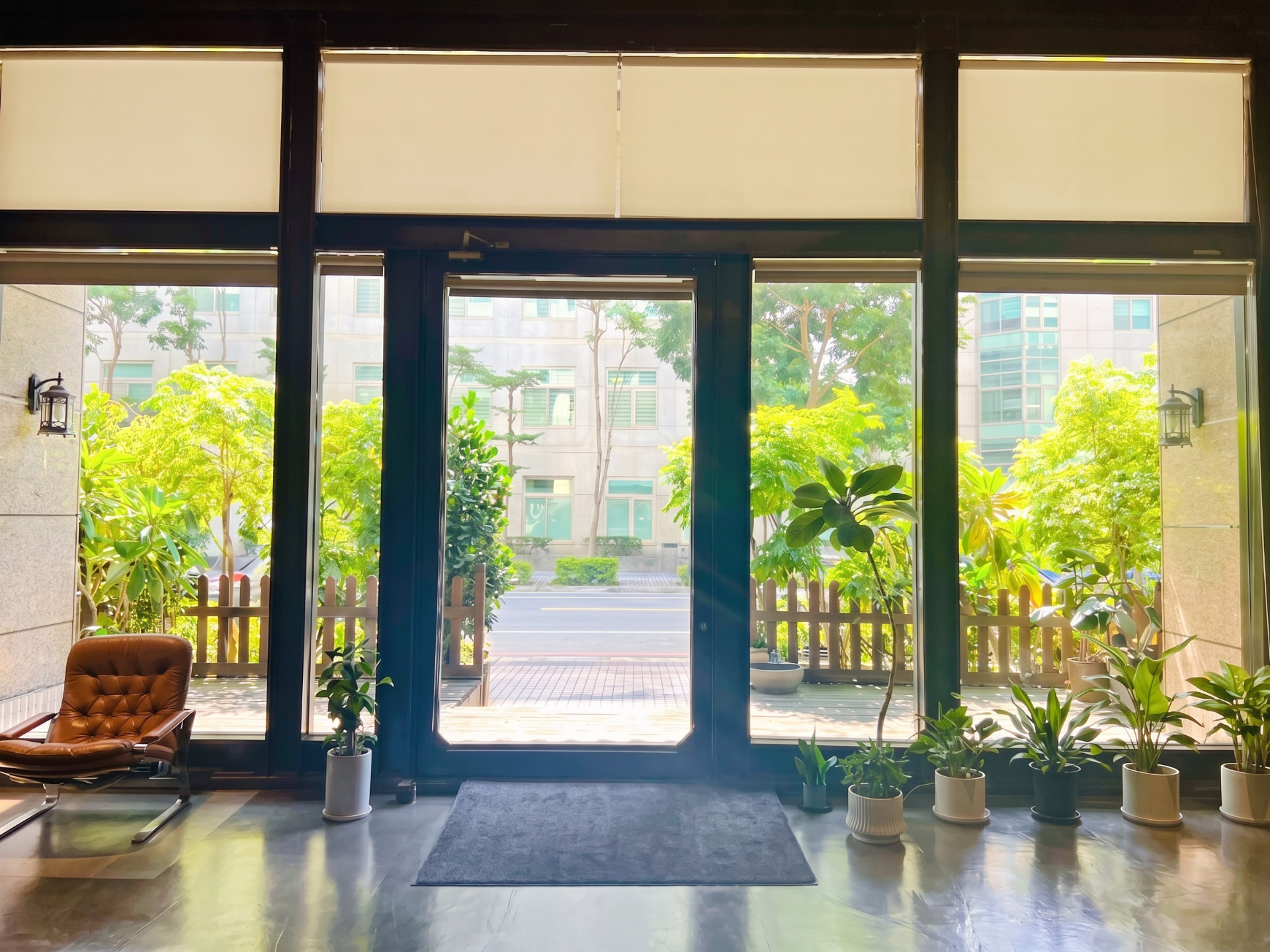 Looking out through the tall glass windows of the A39-1 space: lush greenery, a leather chair, and potted plants in warm light